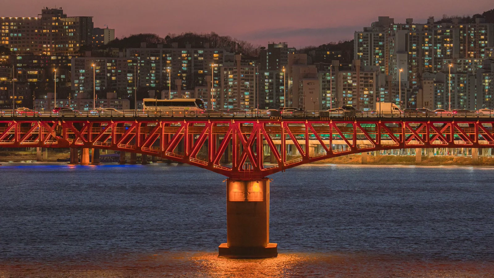 Red illuminated bridge crossing the Hangang River with Seoul apartment towers at dusk