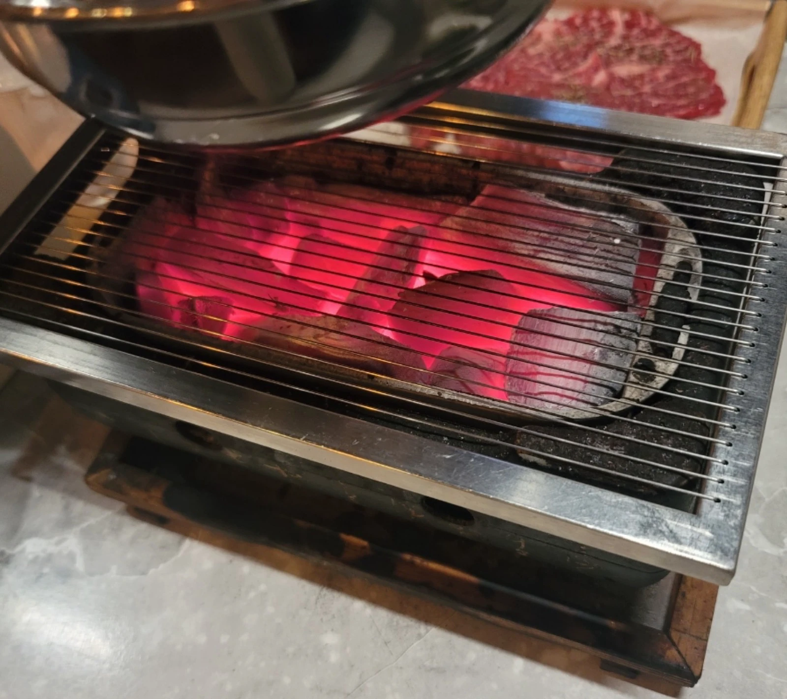 Glowing charcoal in an individual Korean barbecue grill with raw meat on a tray behind it