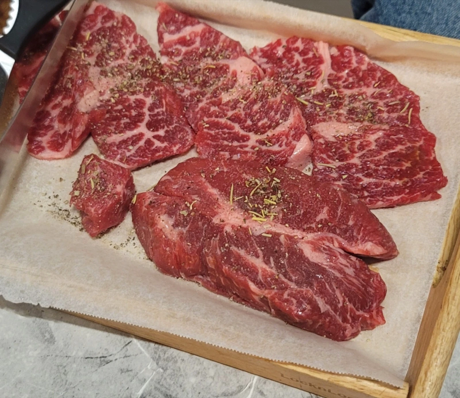 Several raw marbled beef cuts arranged on a wooden tray for Korean barbecue