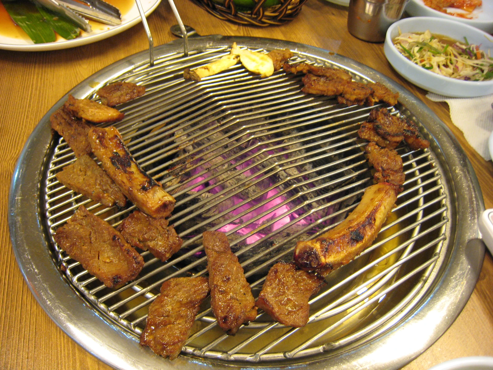 Pieces of cooked galbi arranged around a round Korean tabletop grill