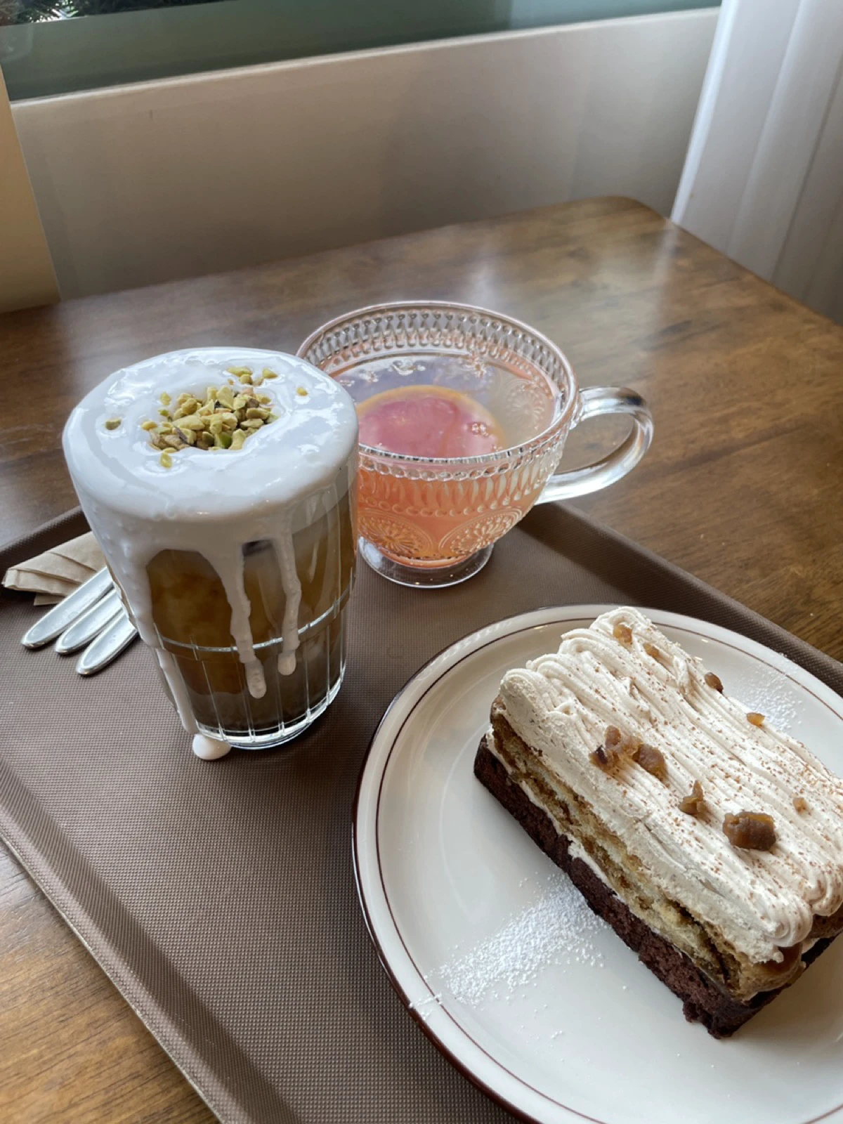 Two drinks beside one rectangular cake on a cafe tray