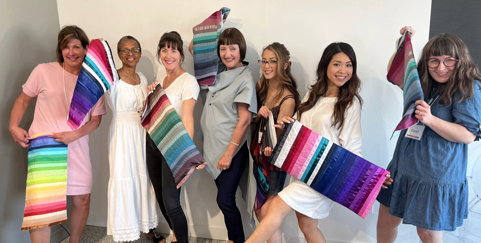 Seven color-analysis trainees with different complexions holding long fabric palettes