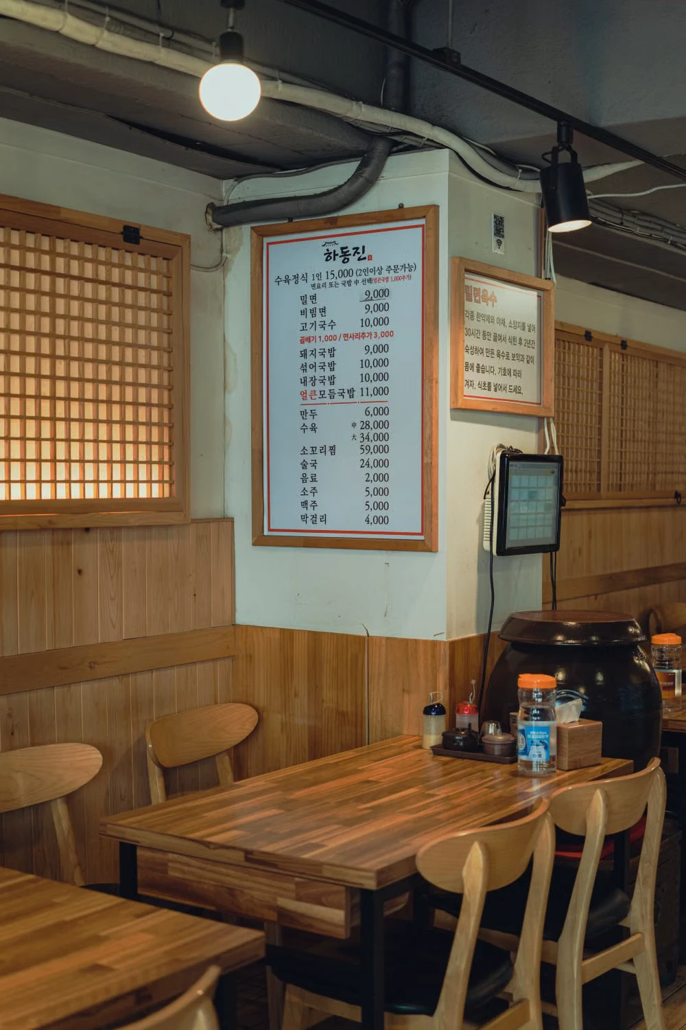 A closer view of the same Korean restaurant showing the menu board, tablet, and table layout