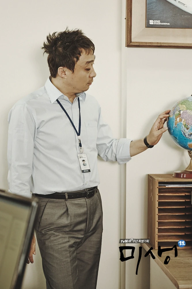 An office employee standing beside a globe in the tvN drama Misaeng