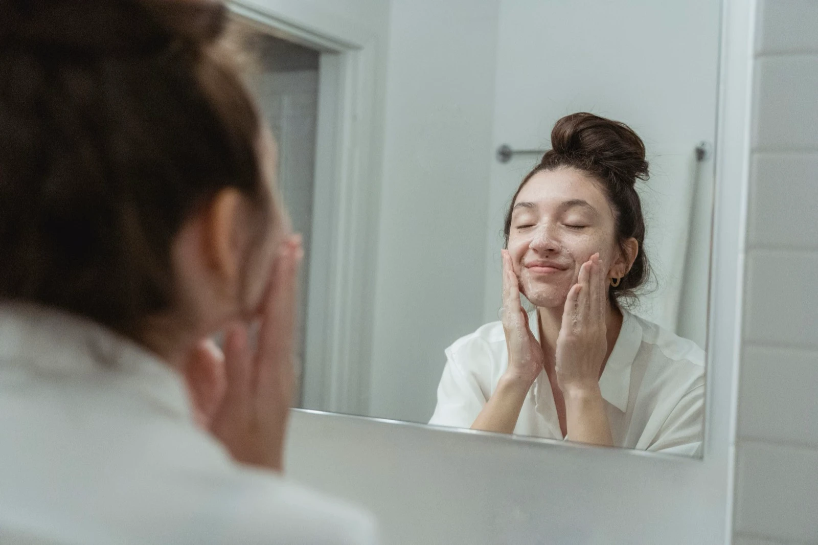 Người phụ nữ nhẹ nhàng rửa mặt bằng đầu ngón tay trước gương phòng tắm