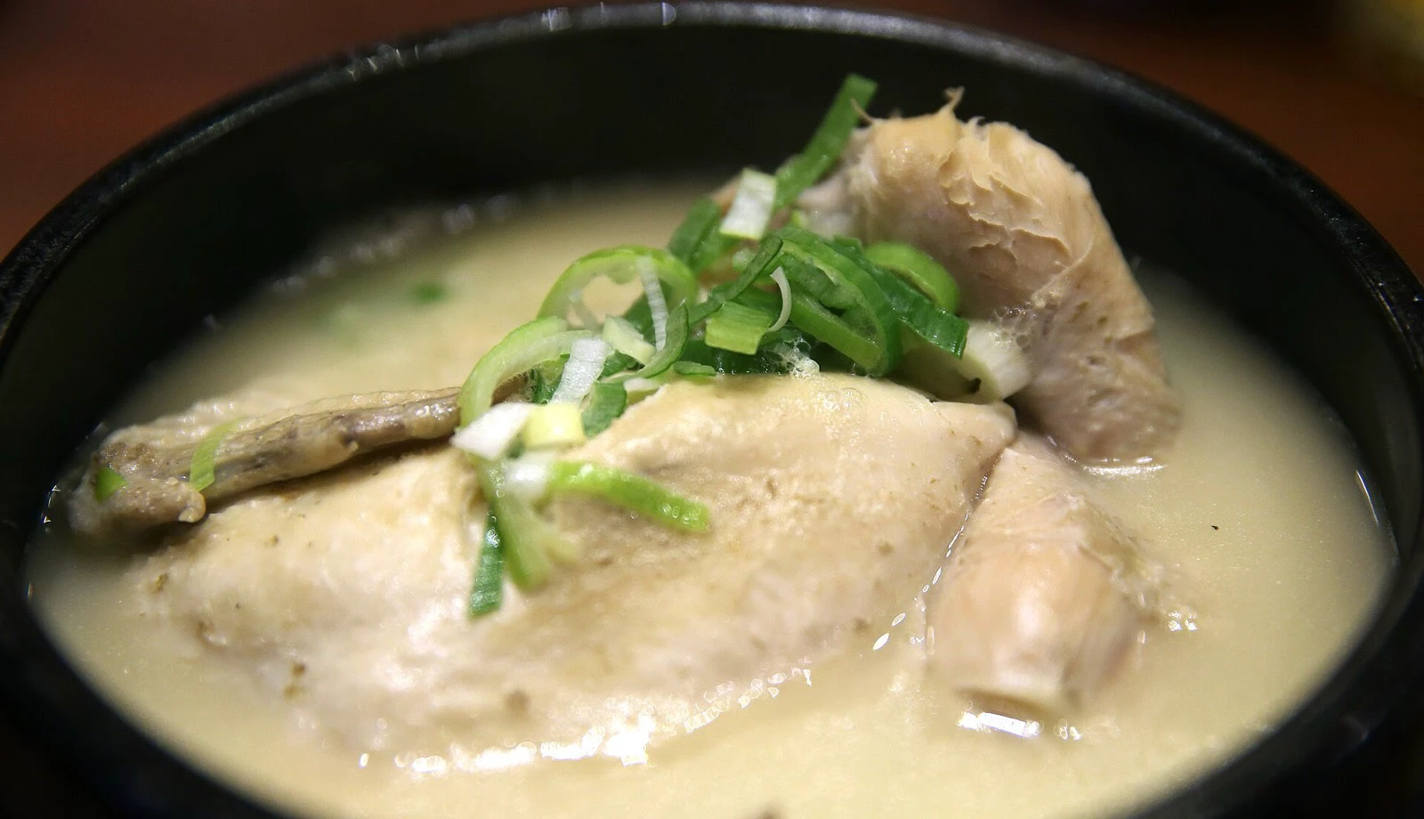 Cận cảnh gà nguyên con trong nước samgyetang nhạt với hành lá