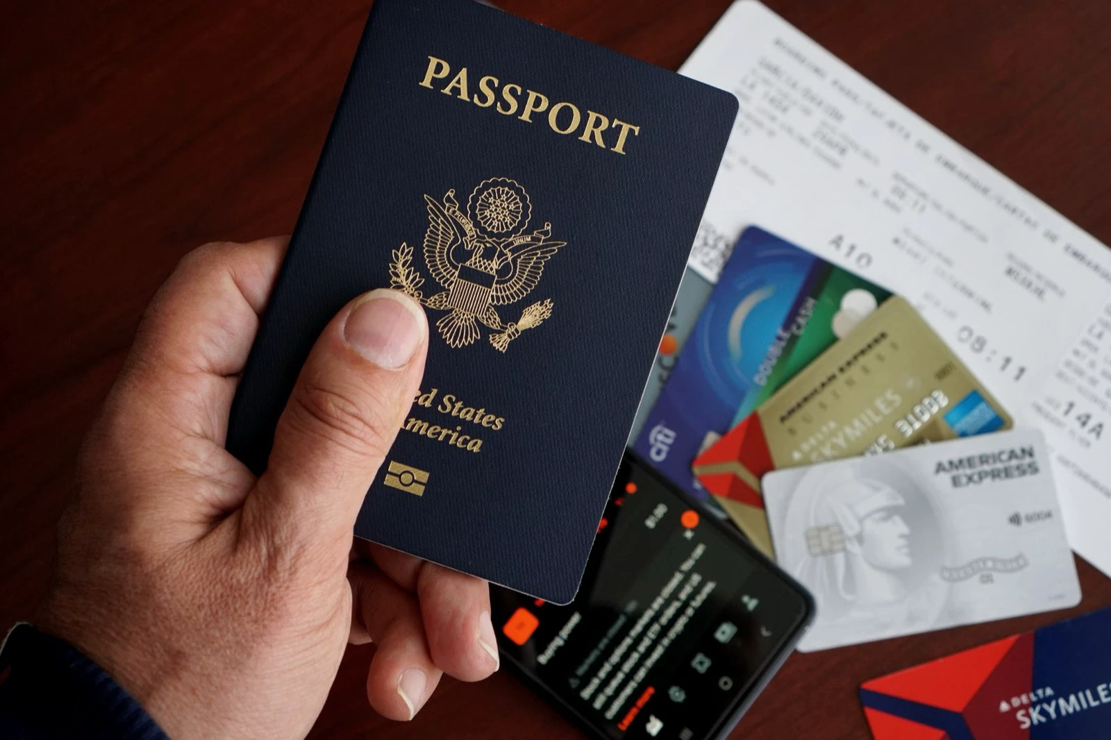 Traveler holding a United States passport above flight documents, bank cards and a phone
