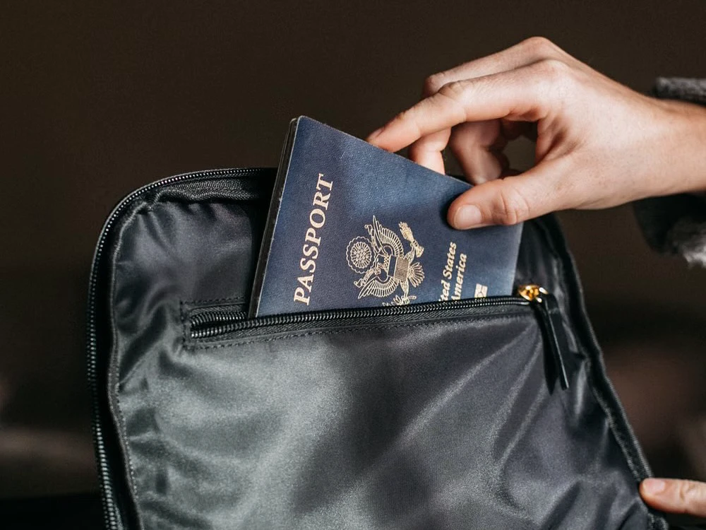 Hand placing a United States passport into a black travel bag