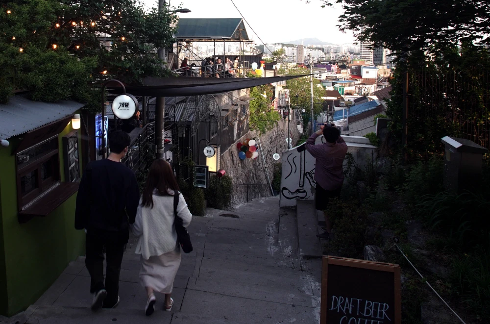 Visitors descending a hillside lane in Ihwa Mural Village as evening lights come on