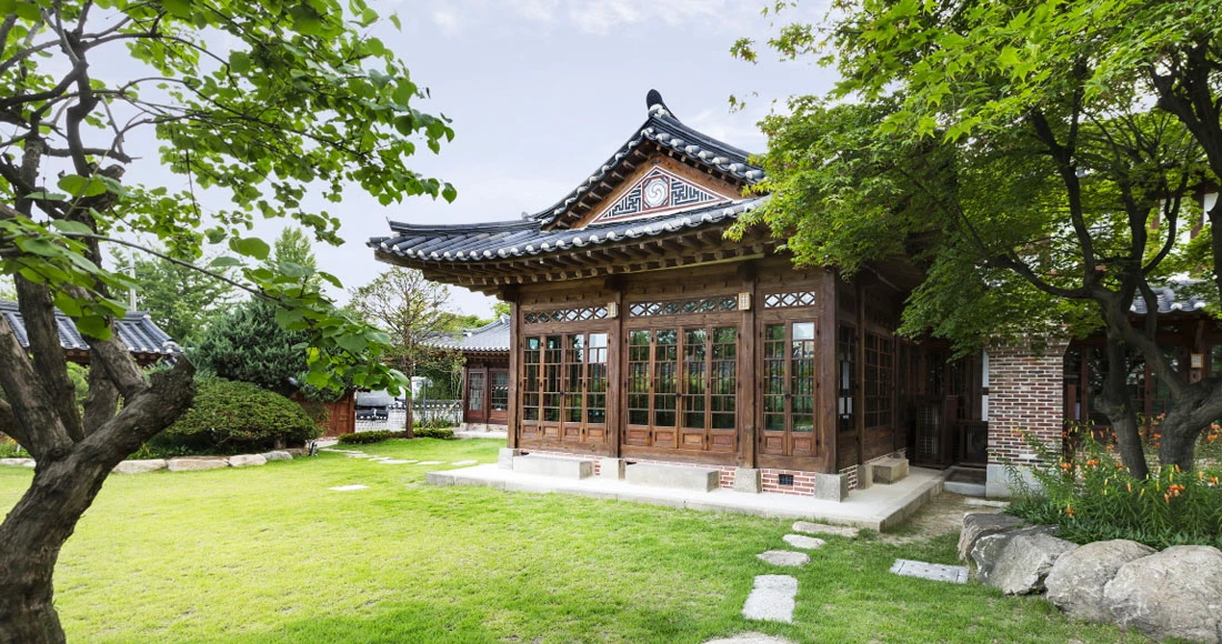 Baek In-je House Museum garden with a glass-fronted hanok framed by leafy trees