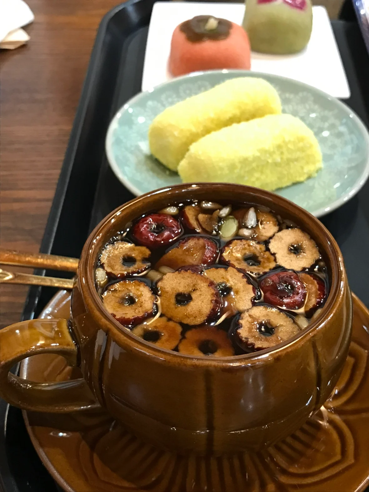 Dark ssanghwa tea topped with sliced jujube and nuts beside pale yellow rice cakes