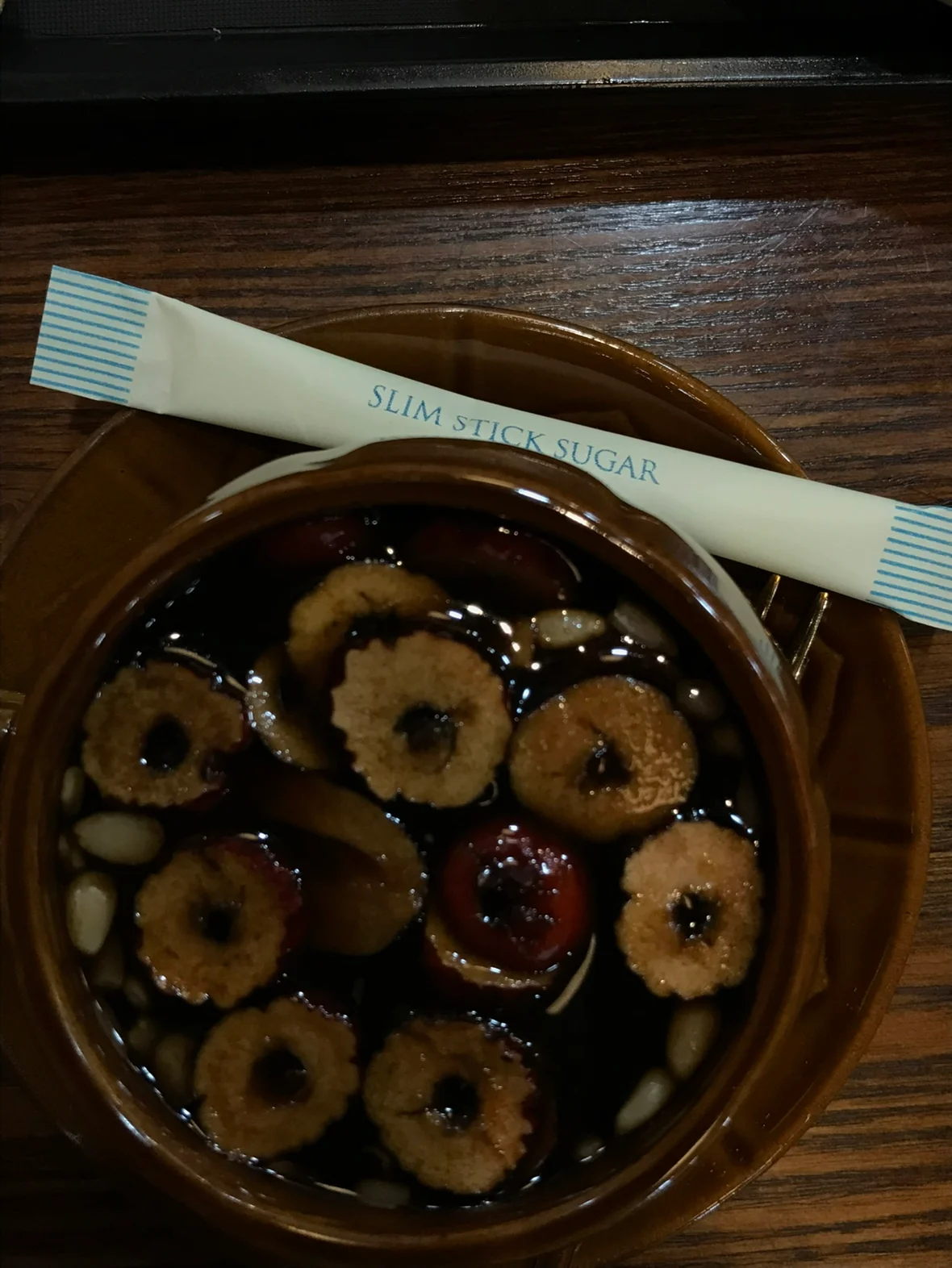 Dark ssanghwa tea topped with sliced jujube, nuts and seeds in a brown ceramic cup