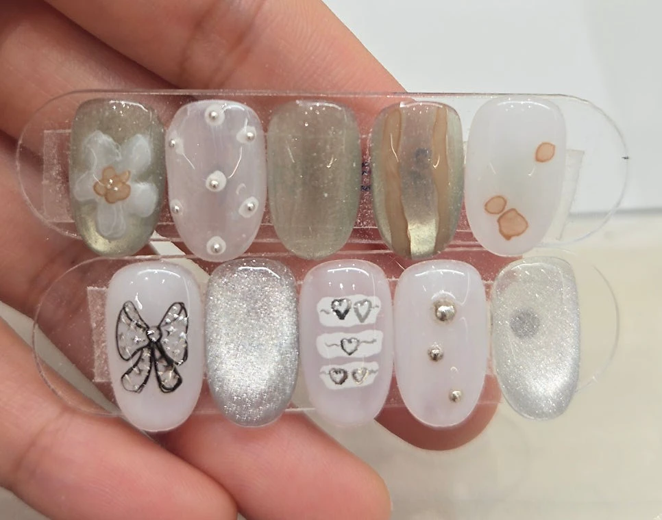 A close-up sample set of pearl, bow, silver and translucent Korean nail-art designs
