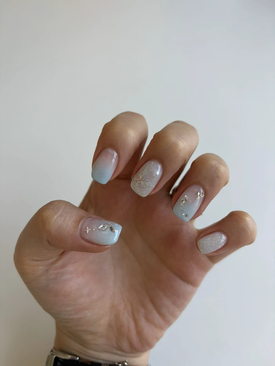 Finished short gel manicure with pale blue gradients, silver glitter and small crystal details