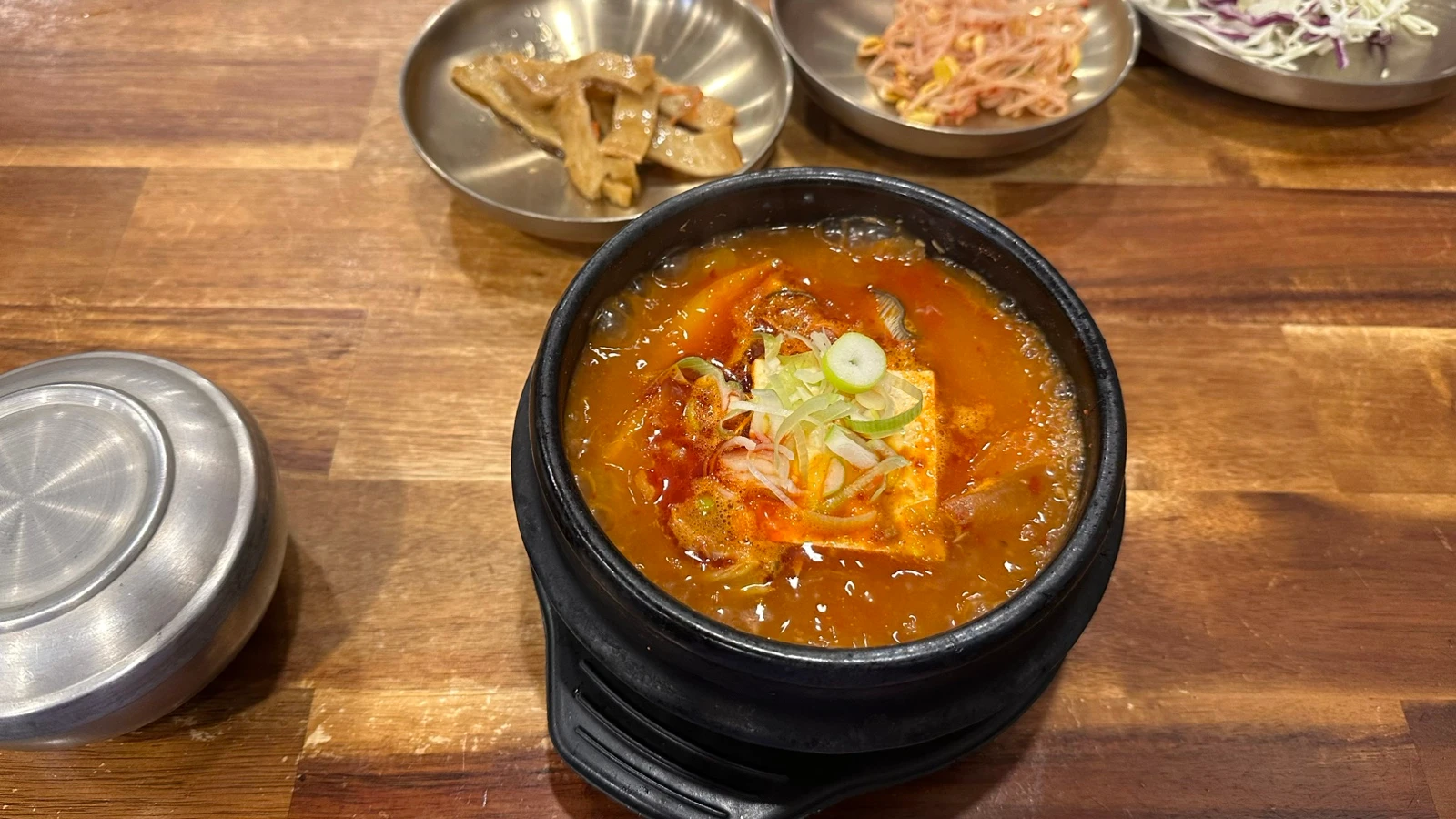 Bubbling halal Korean stew with side dishes on a wooden table at Eid in Itaewon