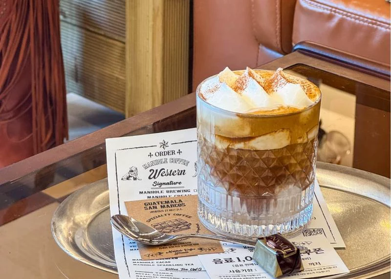 Cà phê phủ kem trên khay cạnh menu Manhole Coffee
