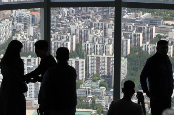 People looking over dense Seoul apartment blocks through a large observation window