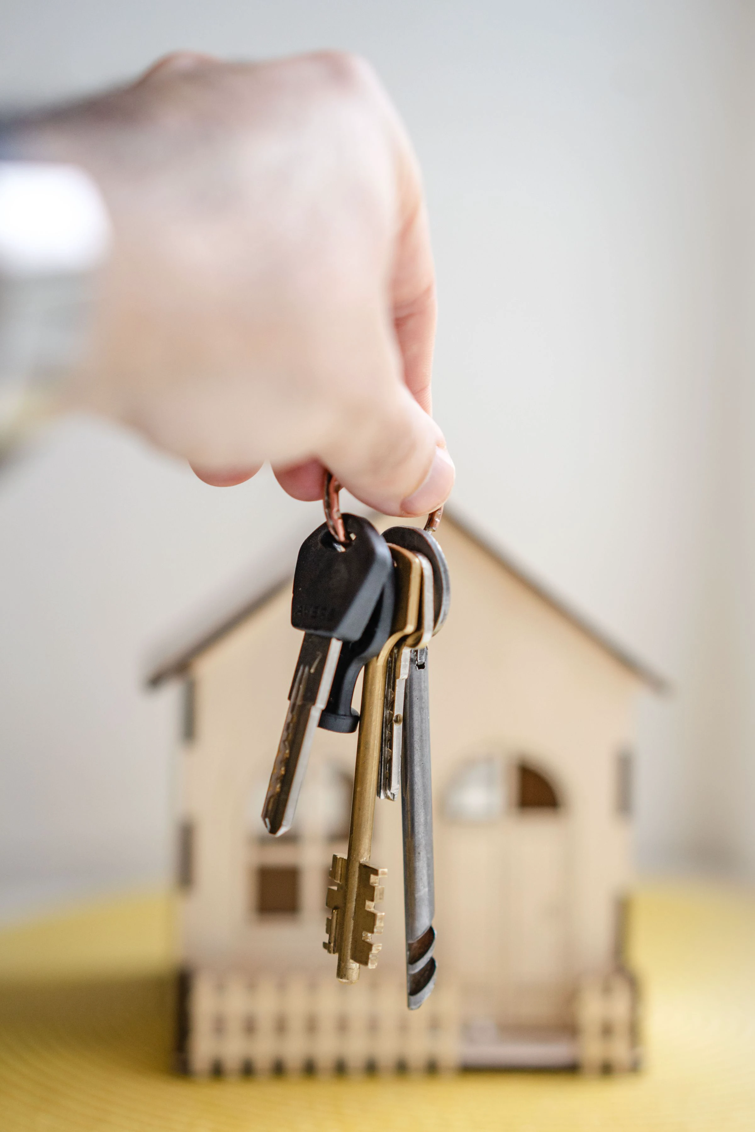 A hand holding house keys in front of a small model home