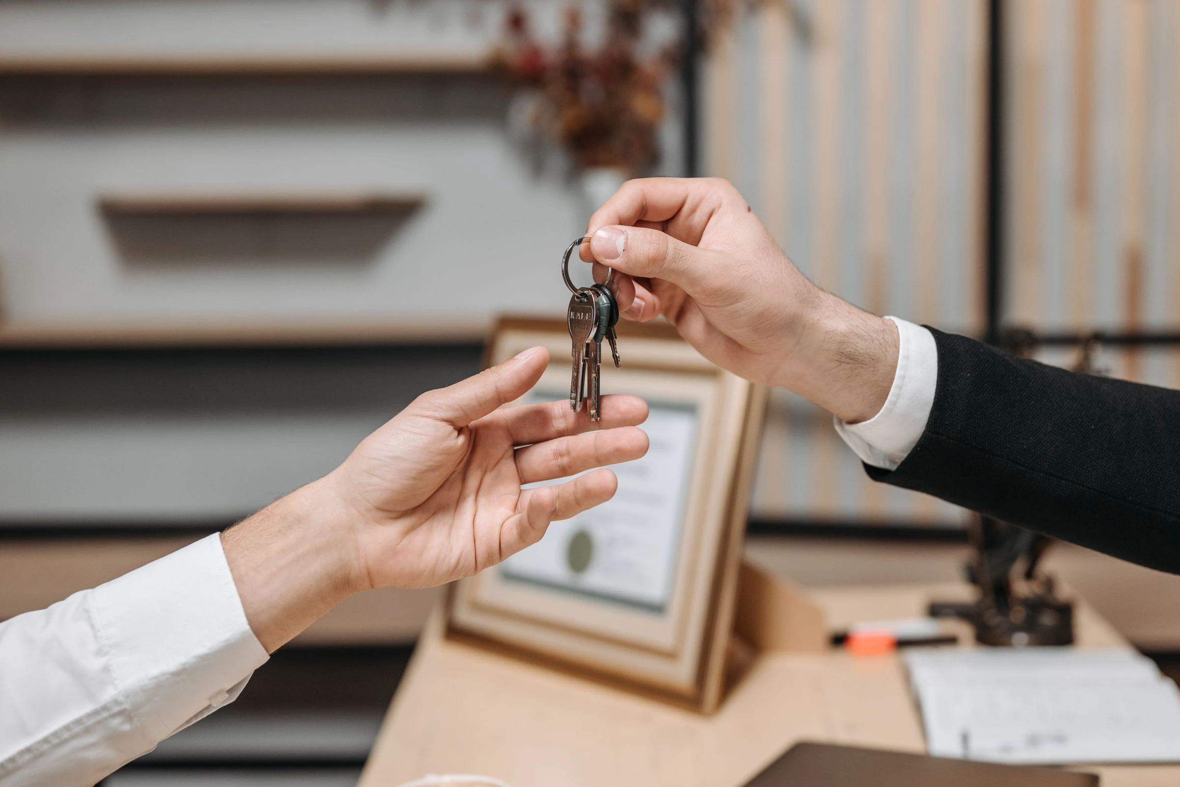 One person handing apartment keys to another across an office desk