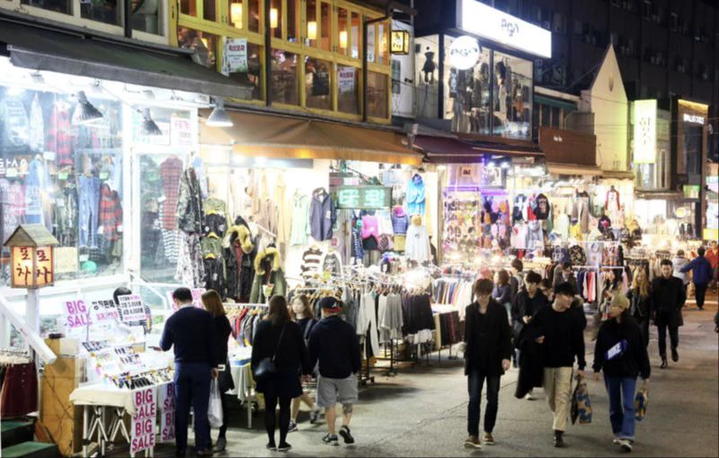 People browsing brightly lit clothing shops along a Hongdae street at night