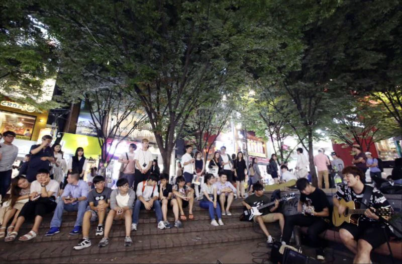 Crowd watching guitarists perform on a stepped plaza in Hongdae at night