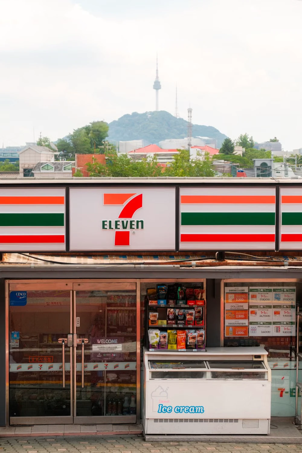 A Seoul 7-Eleven storefront with N Seoul Tower visible behind it
