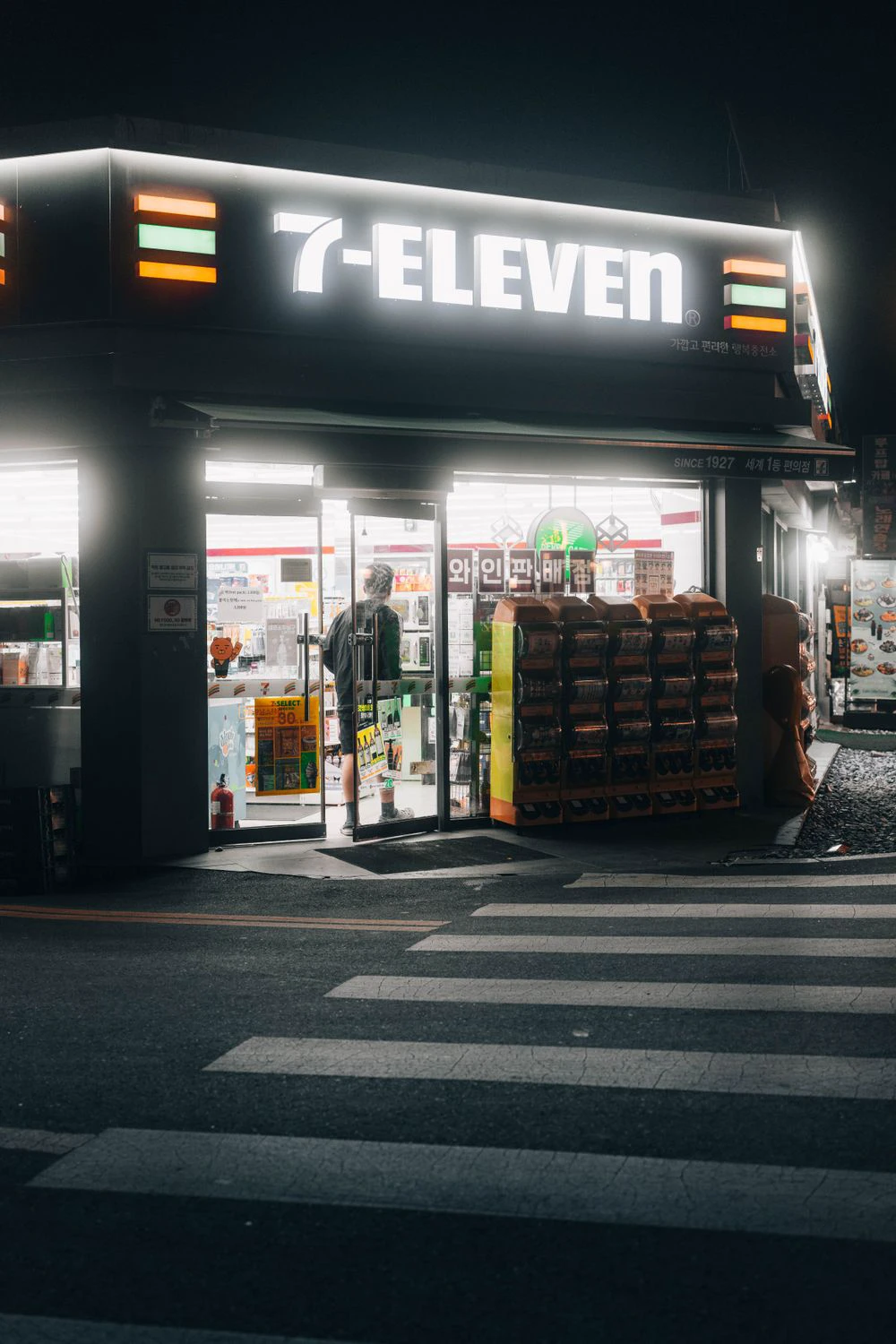 A brightly lit 7-Eleven convenience store on a Seoul street at night