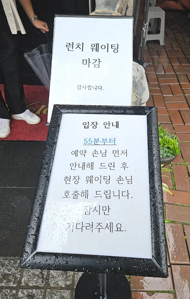 Rain-speckled Korean restaurant signs saying lunch waiting is closed and reservations are seated before walk-ins
