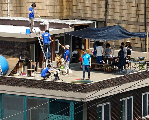 Korean rooftop room surrounded by an exposed flat roof, shade canopy, and volunteers