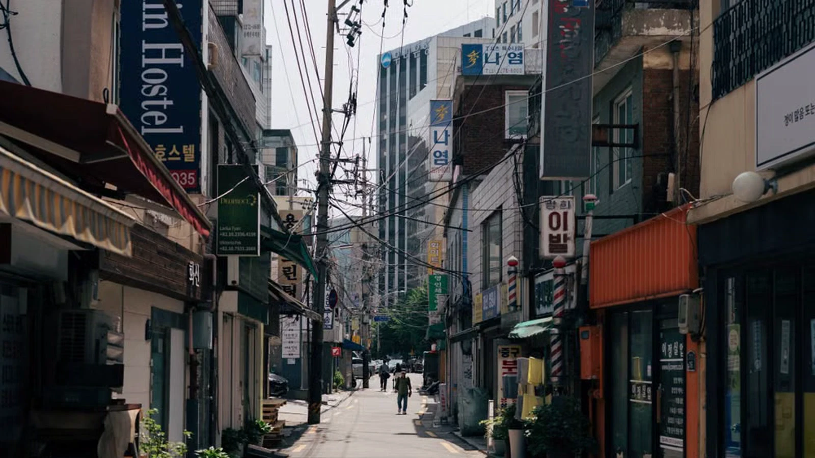 A sunlit narrow street in central Seoul with exposed pavement and pedestrians in the distance