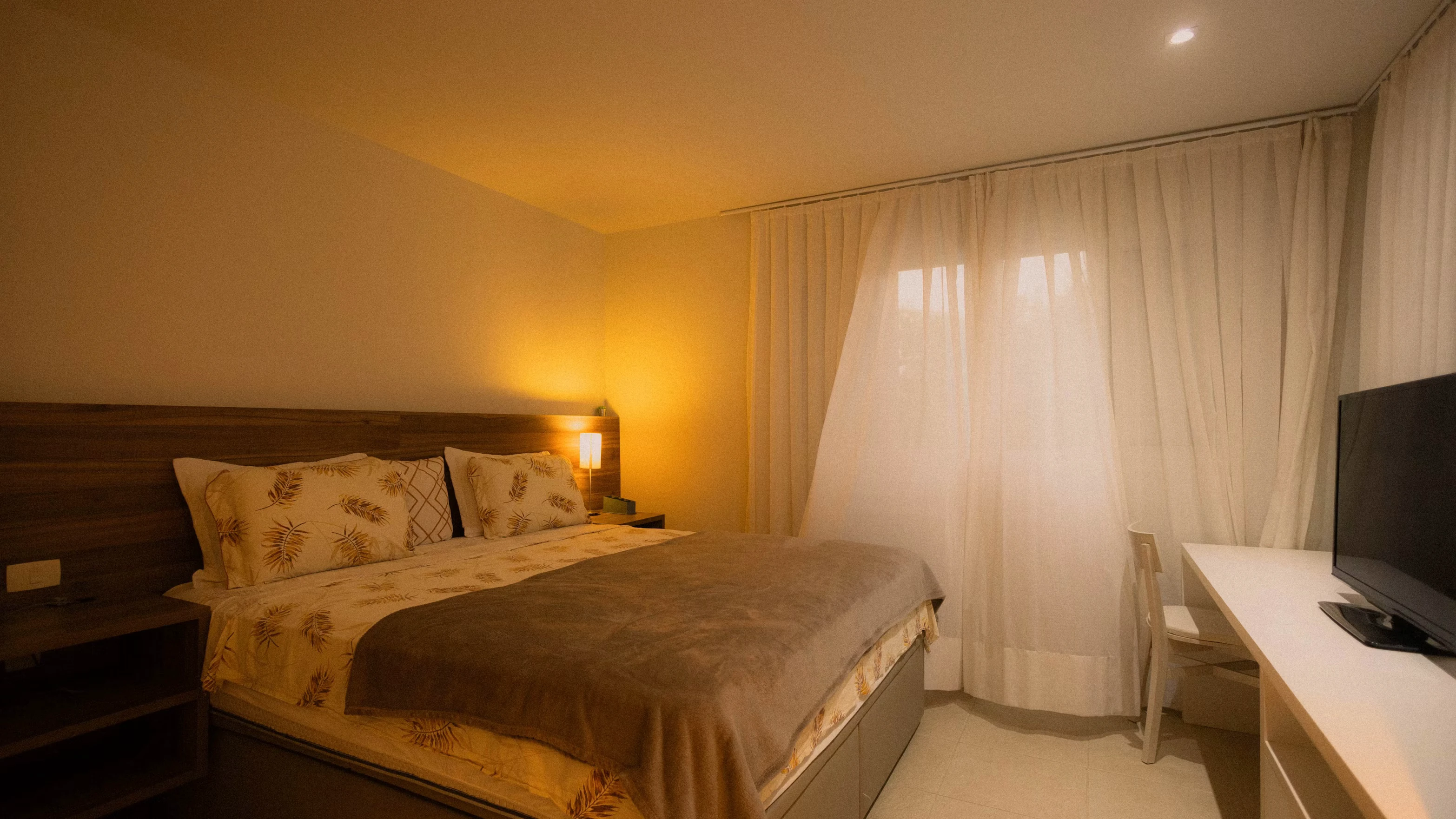 Kamar hotel modern bernuansa hangat dengan tempat tidur rapi dan televisi