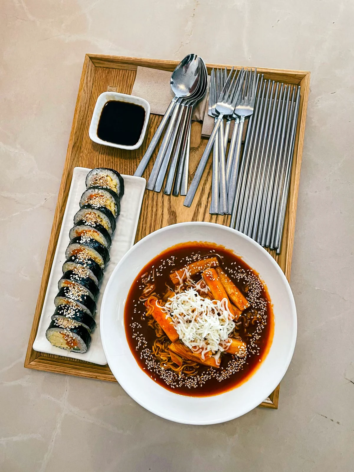 Tray with sliced gimbap and a bowl of spicy tteokbokki topped with shredded cheese