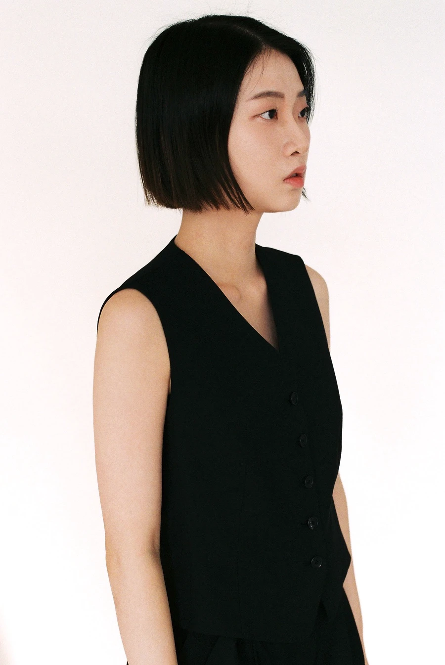Side view showing the cropped length and arm opening of a black buttoned vest