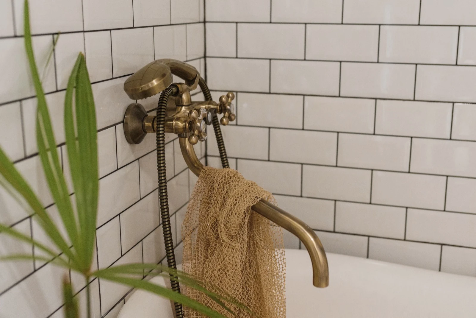 Vintage brass handheld shower and faucet mounted above the rim of a bathtub