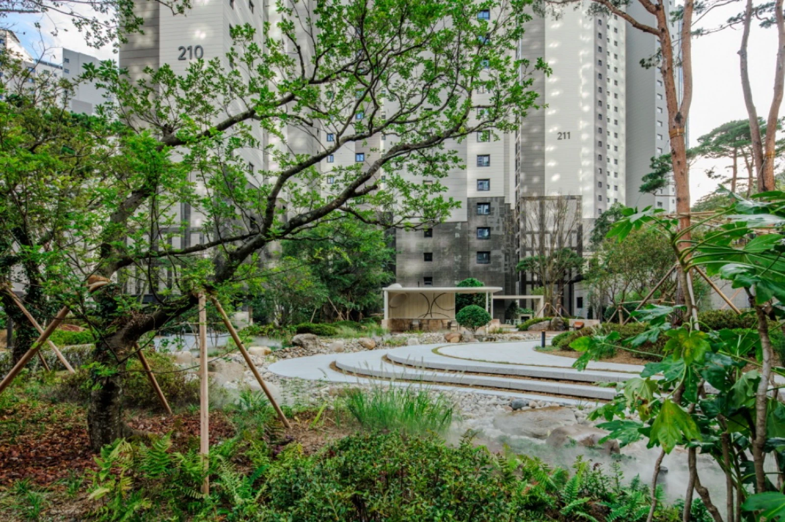 Rain garden framed by apartment towers and mature trees at Raemian Forestige