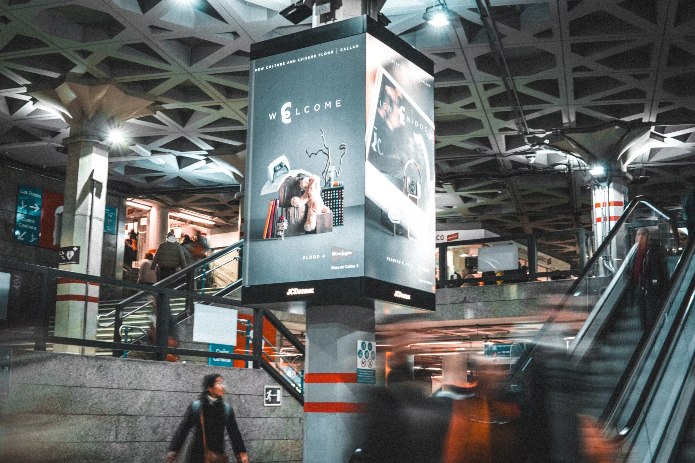 Billboard besar menyala di atas eskalator sebuah stasiun metro yang ramai