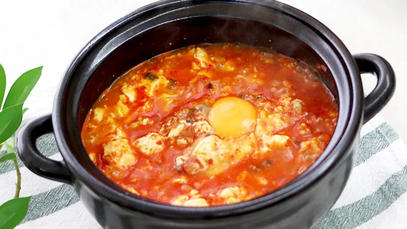 Pork sundubu jjigae with soft tofu and an egg in a black handled pot