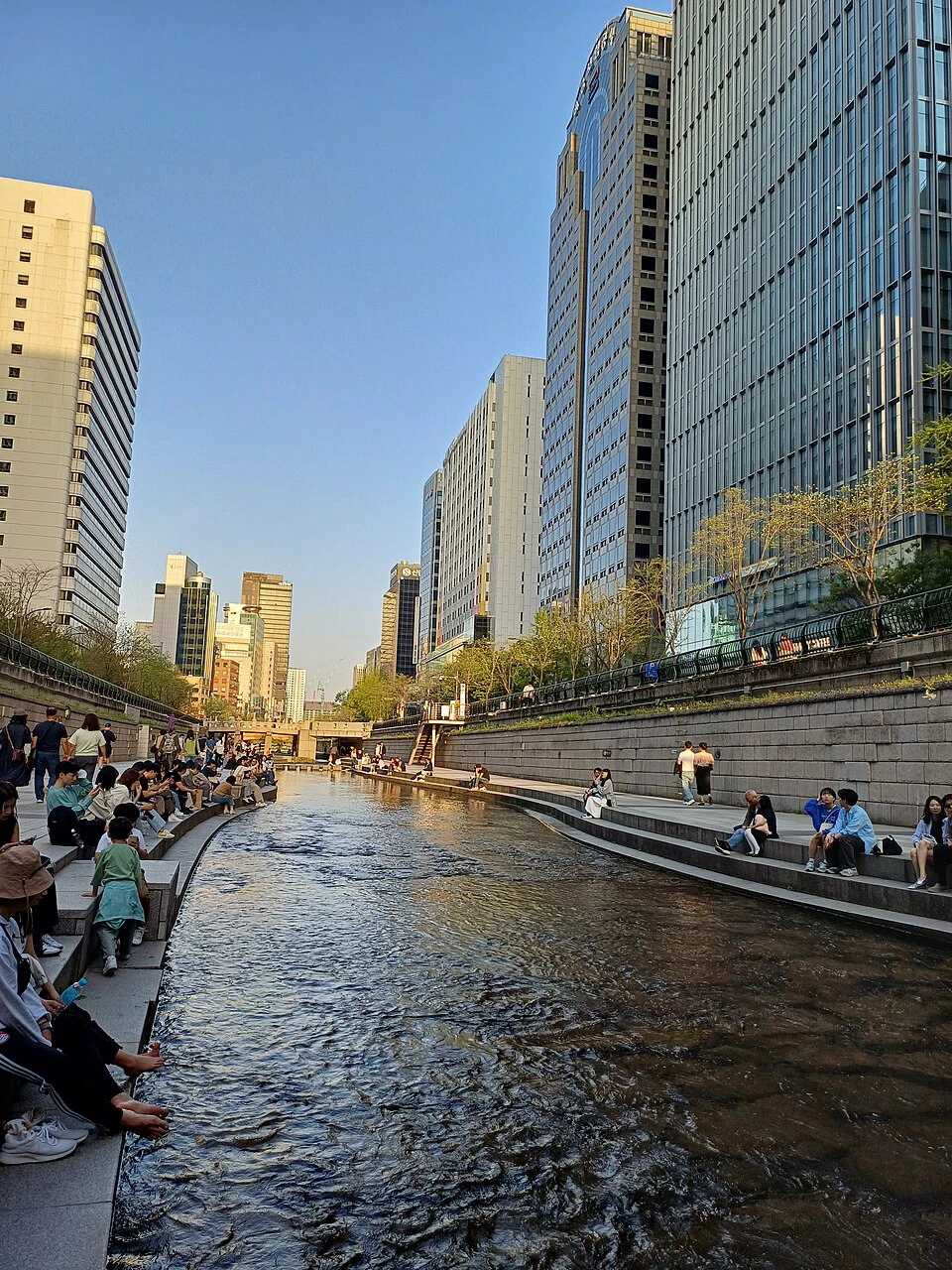 People resting beside Cheonggyecheon Stream in the low evening sun