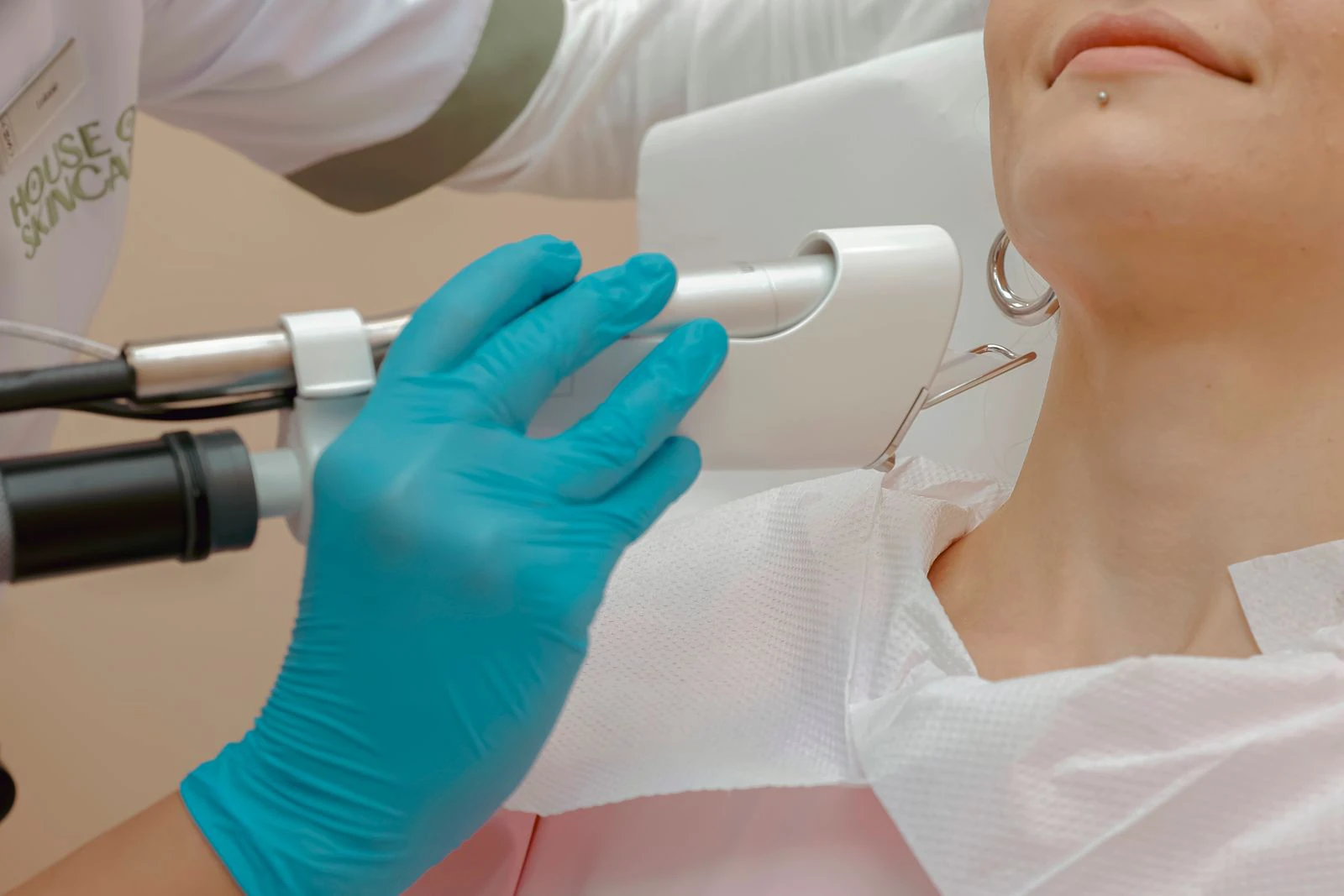 Gloved practitioner positioning a laser handpiece near a patient's lower face in a treatment room
