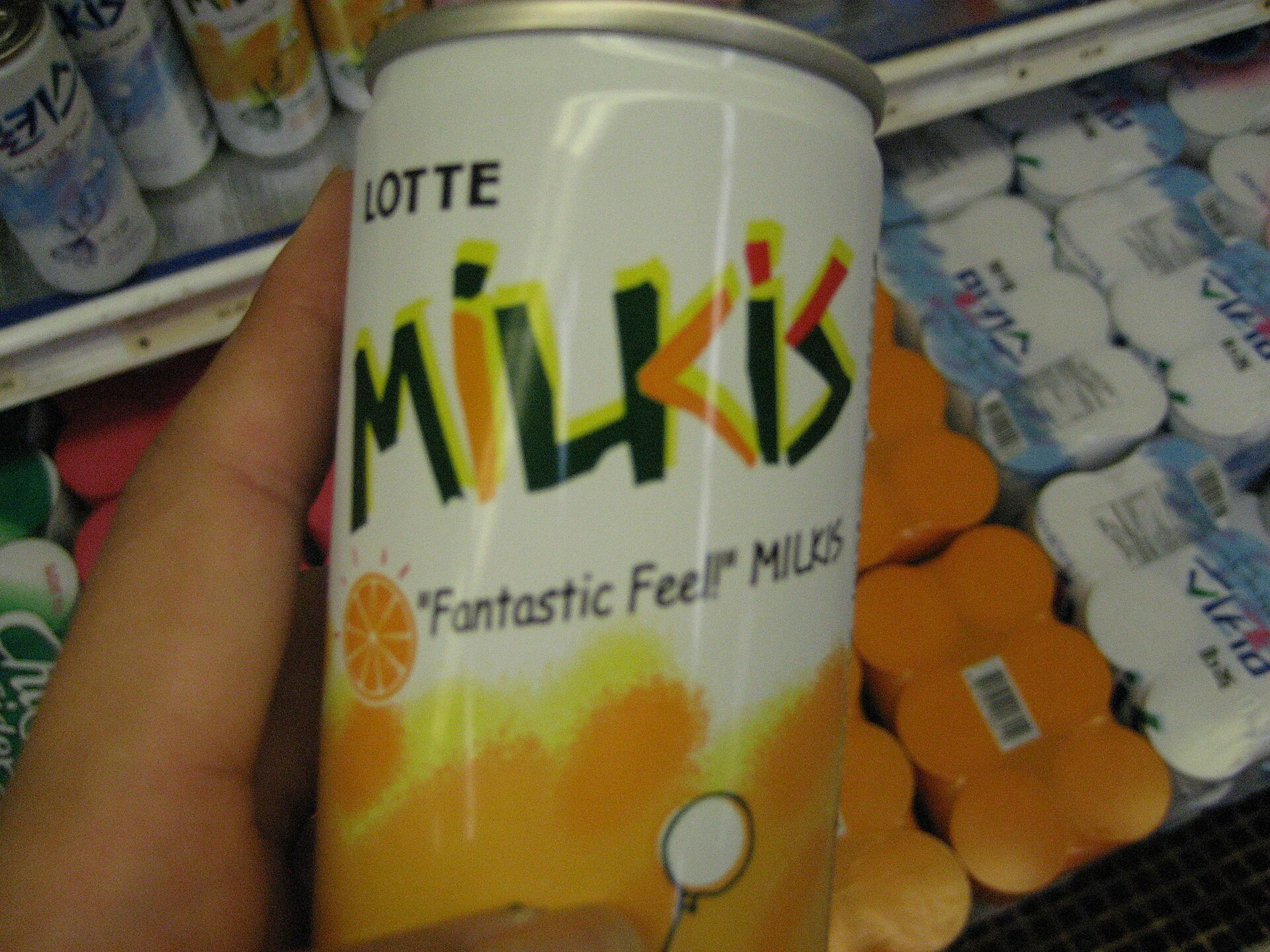 Older citrus-flavored Milkis can held in front of a refrigerated drink case
