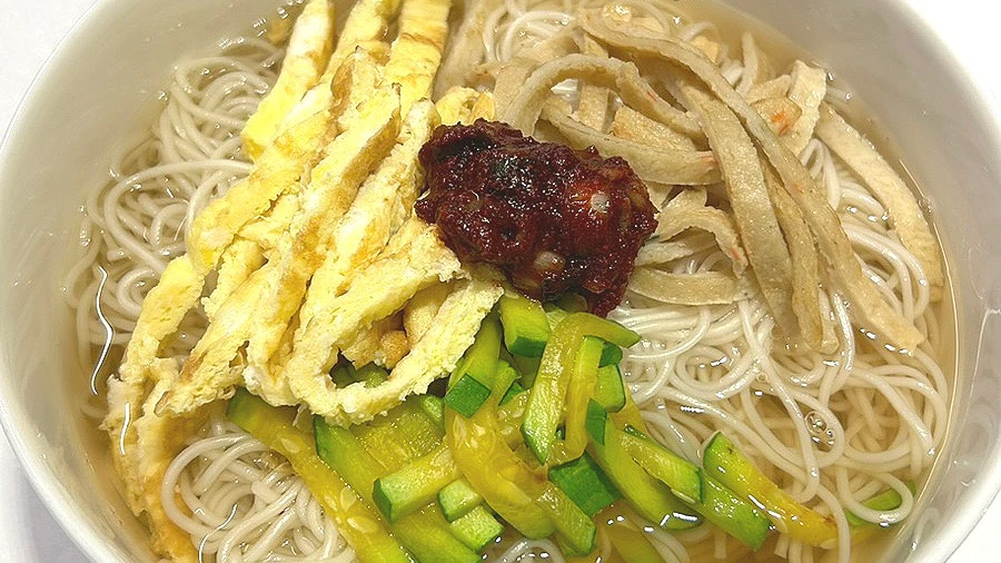 Janchi guksu in clear broth topped with egg strips, zucchini, and red seasoning