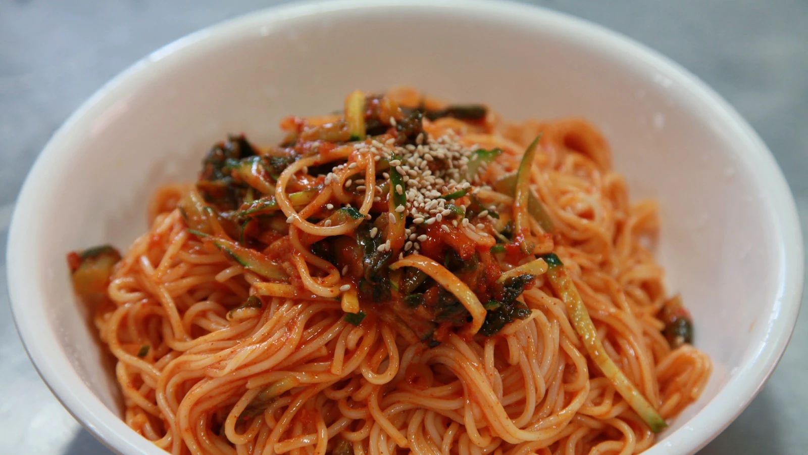 Cold bibim guksu coated in red spicy-sweet sauce with cucumber and sesame seeds