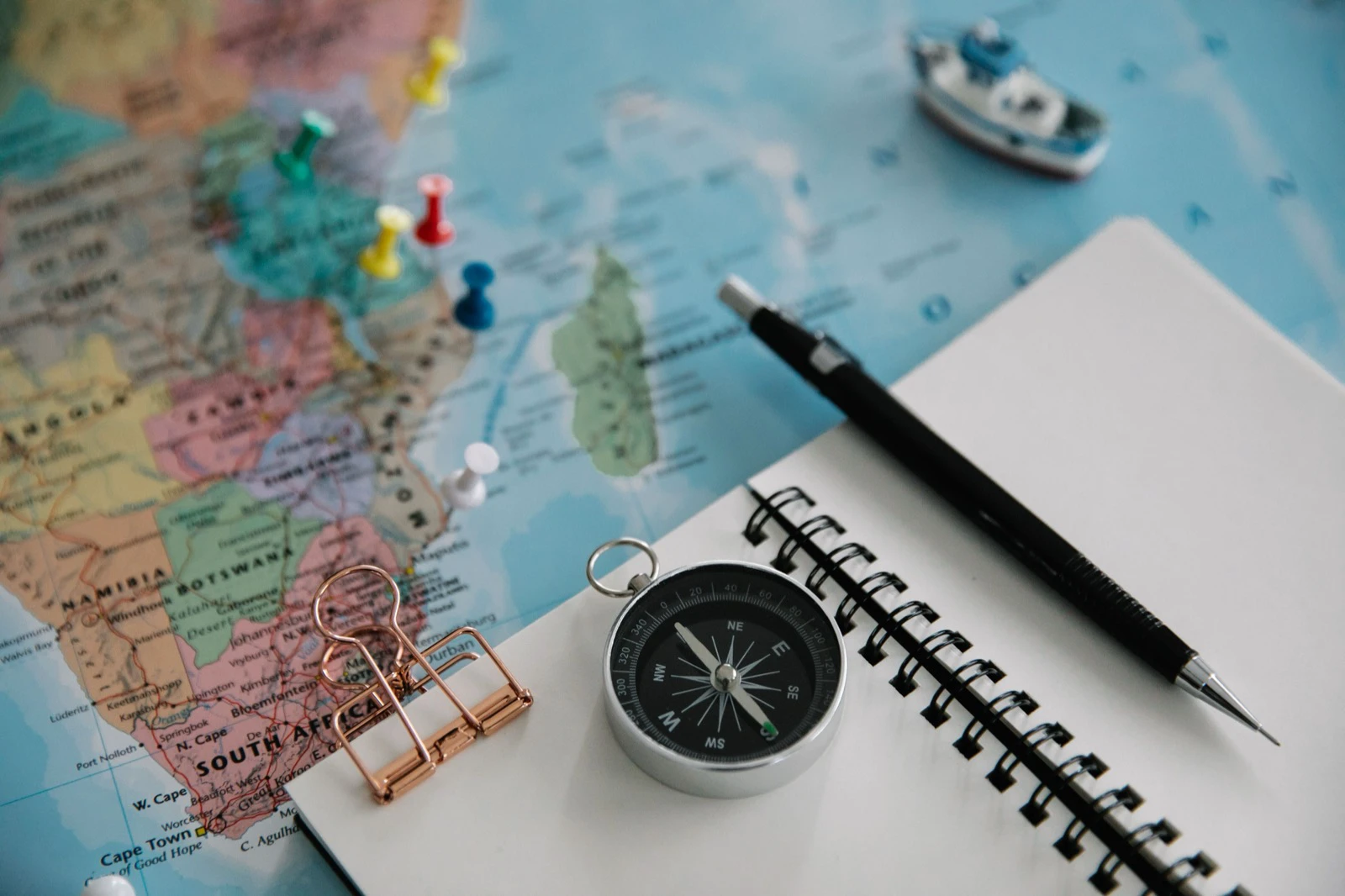 Map, notebook, compass, pen, and pins arranged for planning a travel itinerary