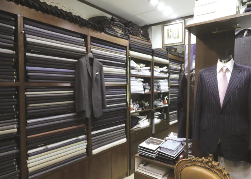 Shelves filled with folded suit cloth beside a finished pinstripe jacket in a Seoul tailor shop