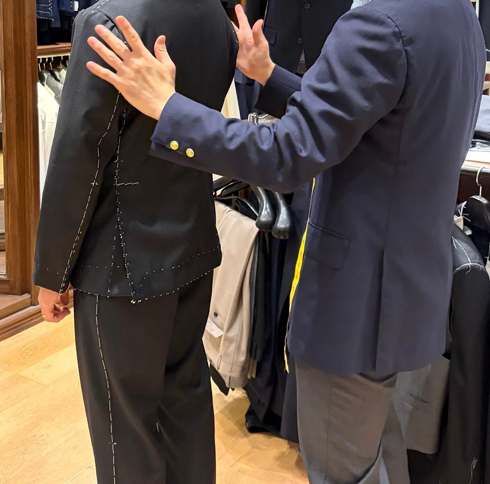 Tailor assessing the back and shoulder of a customer wearing a basted black suit