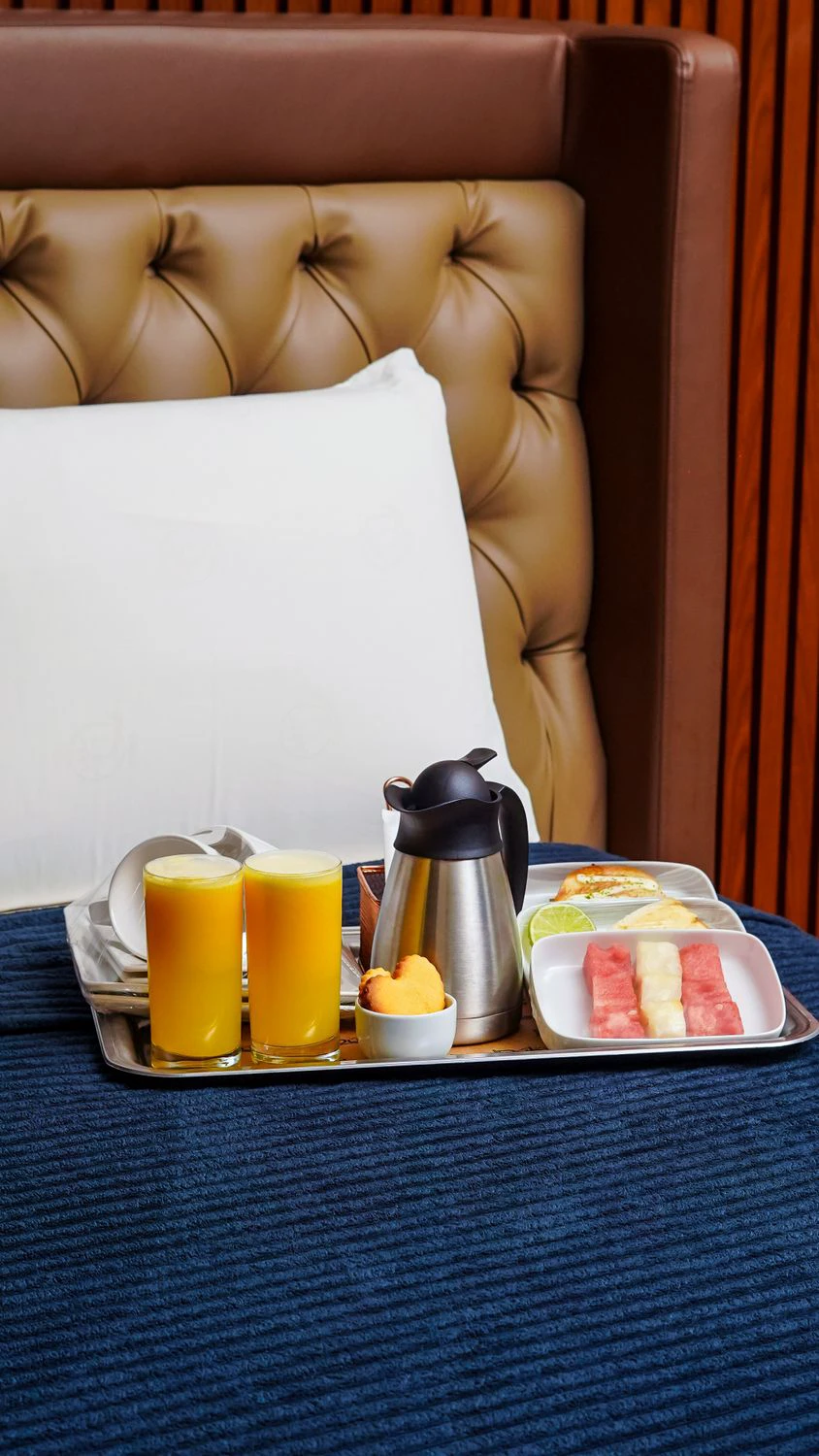 Breakfast tray with fruit, juice, coffee, and bread set on a hotel bed