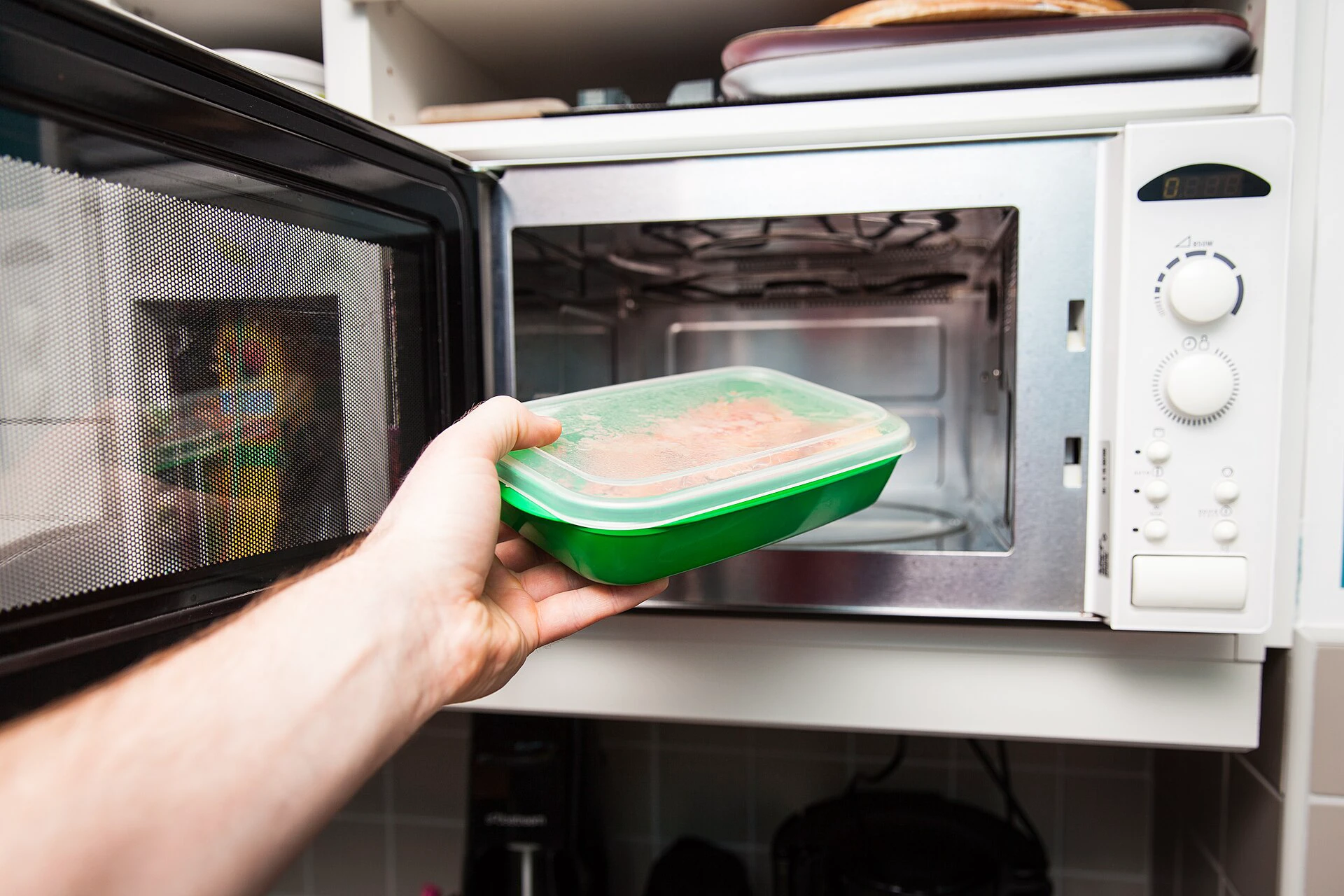Hand placing a covered food container into an open microwave oven
