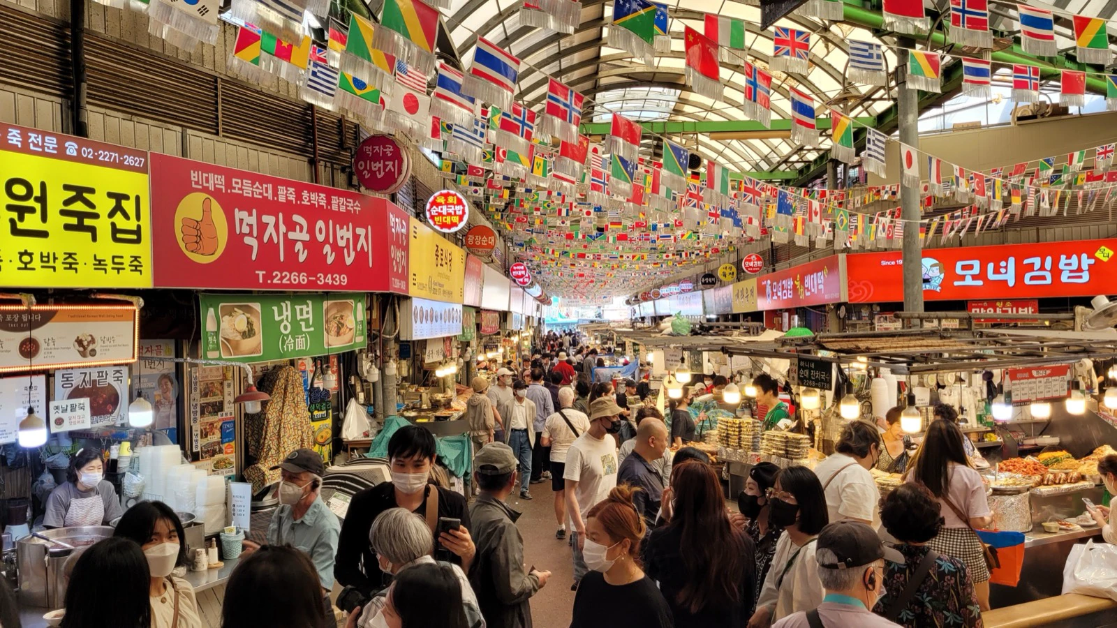 Crowded food aisle under colorful flags inside Gwangjang Market in Seoul