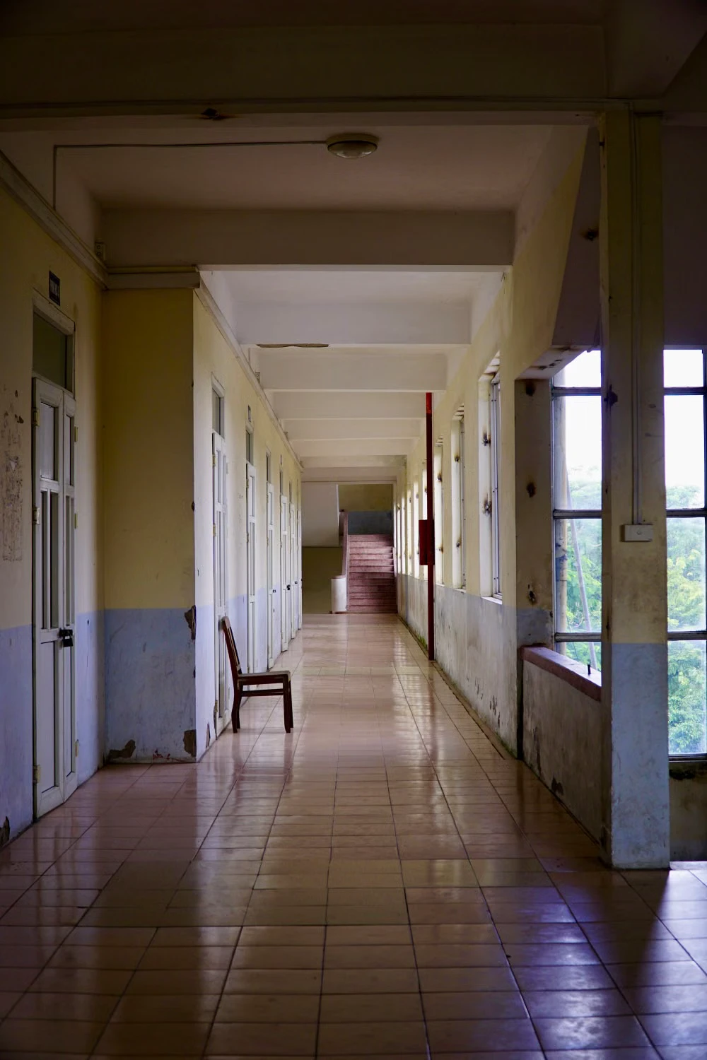 Koridor sekolah yang kosong dan temaram, dengan satu kursi serta garis perspektif memanjang