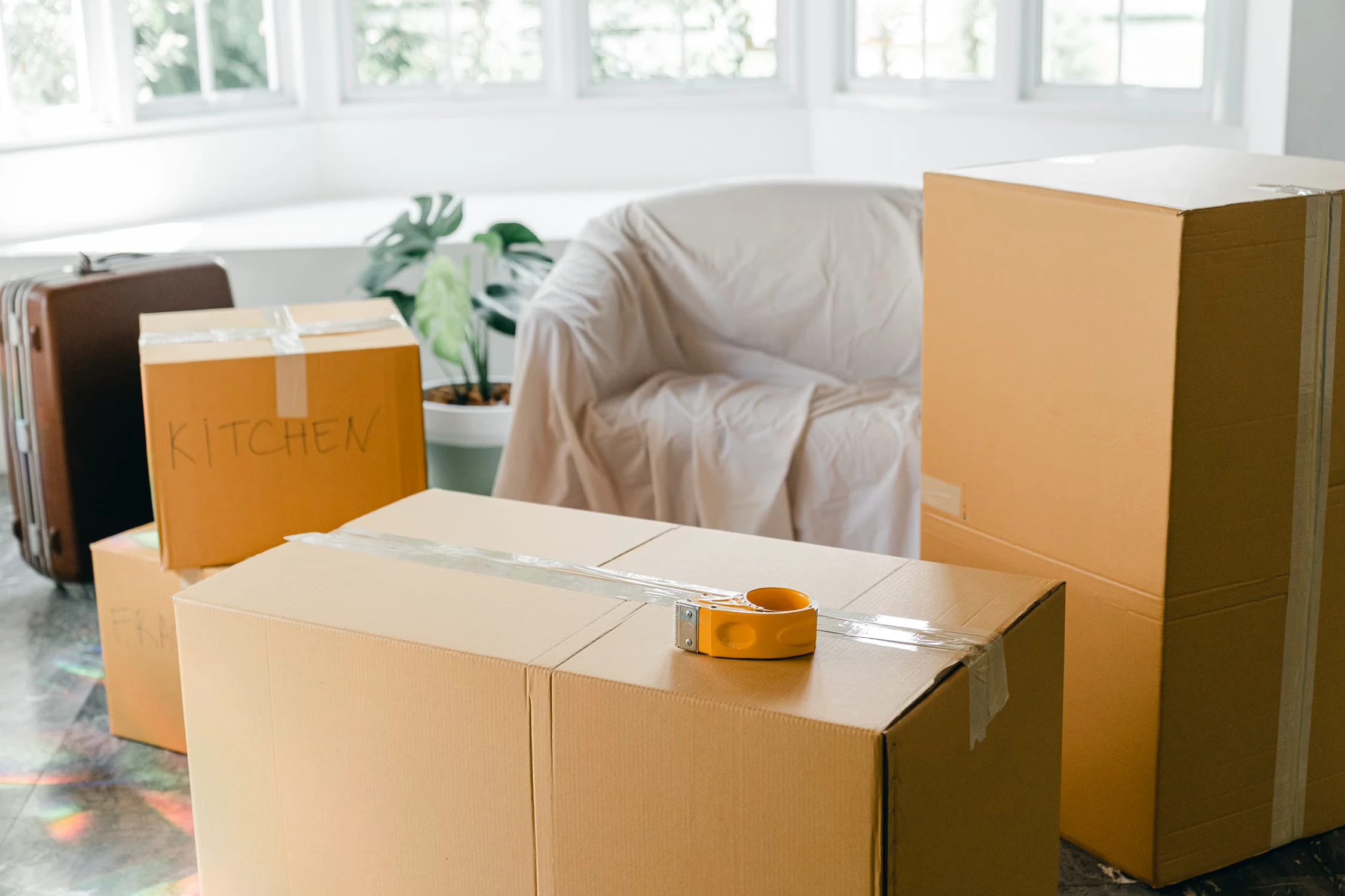 Sealed moving boxes, tape and a suitcase in a bright room ready for relocation